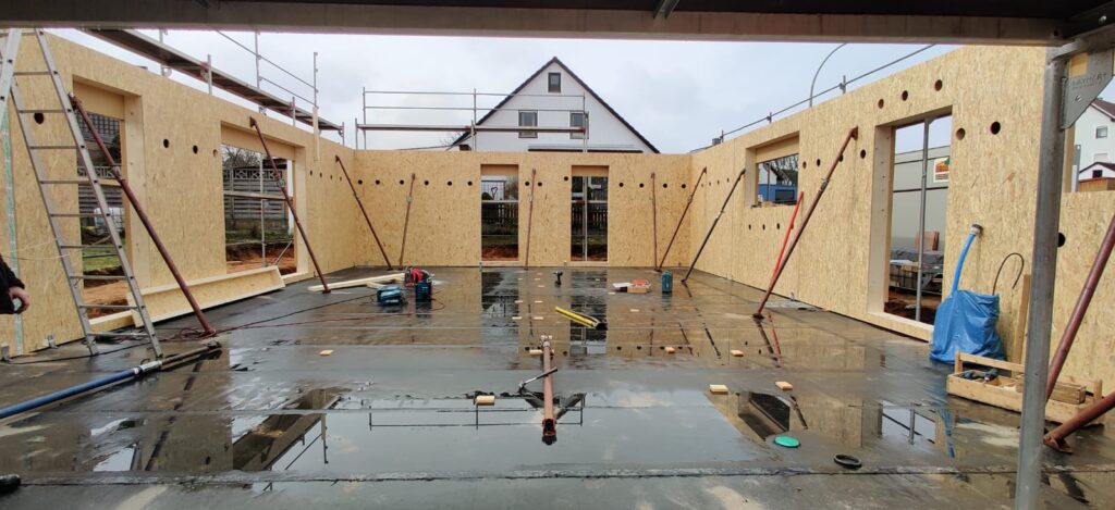 Eine Bodenplatte von einem Haus mit drei Fertigwänden aus Holz.